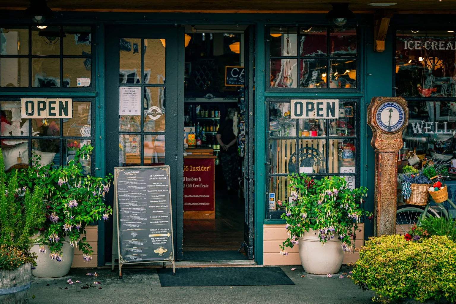 A green shopfront with open signs and potted plants by the door.
