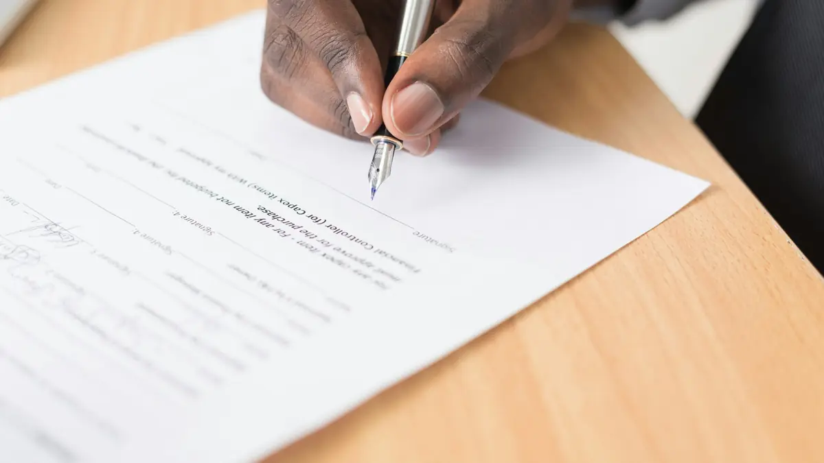A hand signing a printed document with a fountain pen.