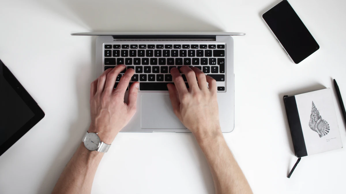 Hands typing on a laptop on a white desk, seen from above.